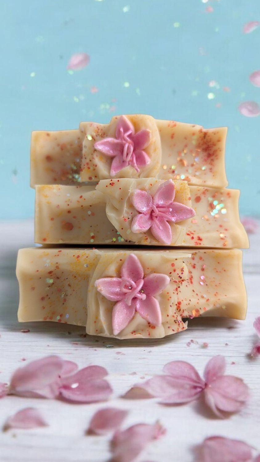 Rustic Sakura Soap Stack of three soaps adorned with floral decorations and pink petals on a light blue background.