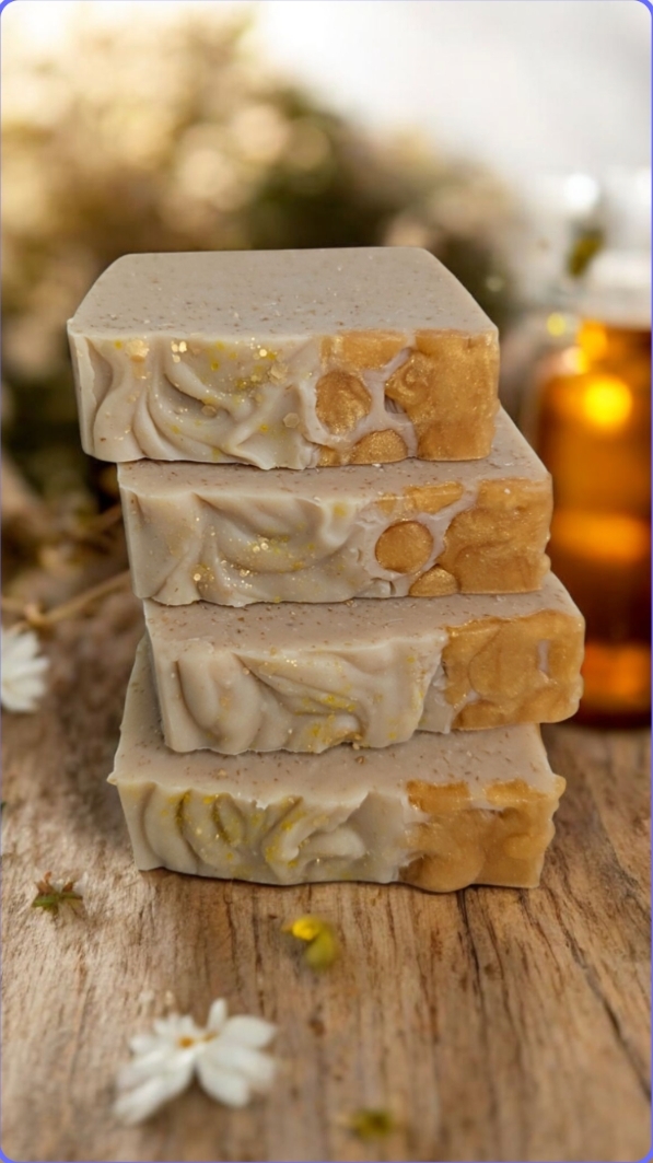 Four stacked bars of handmade soap with a floral pattern, next to a bottle.
