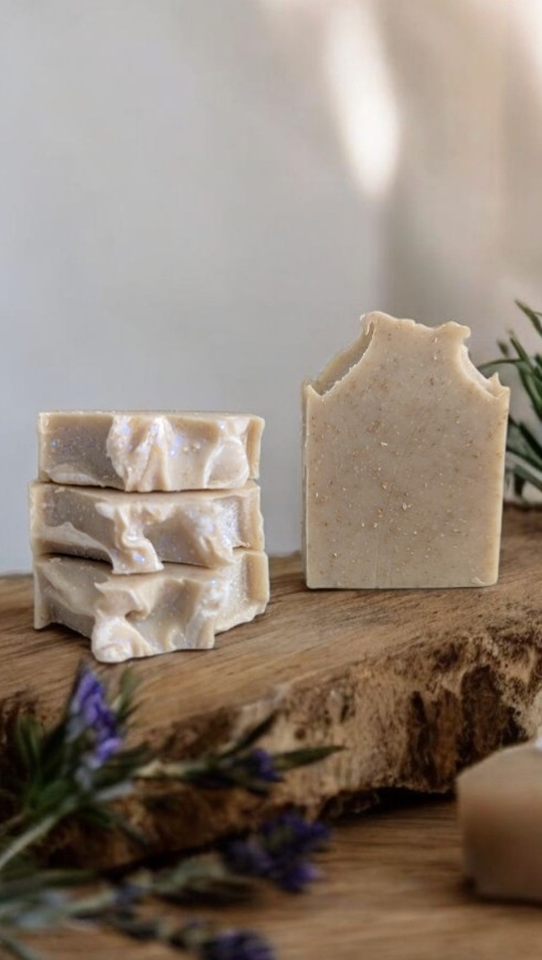 Handmade soap bars near greenery on a wooden surface.