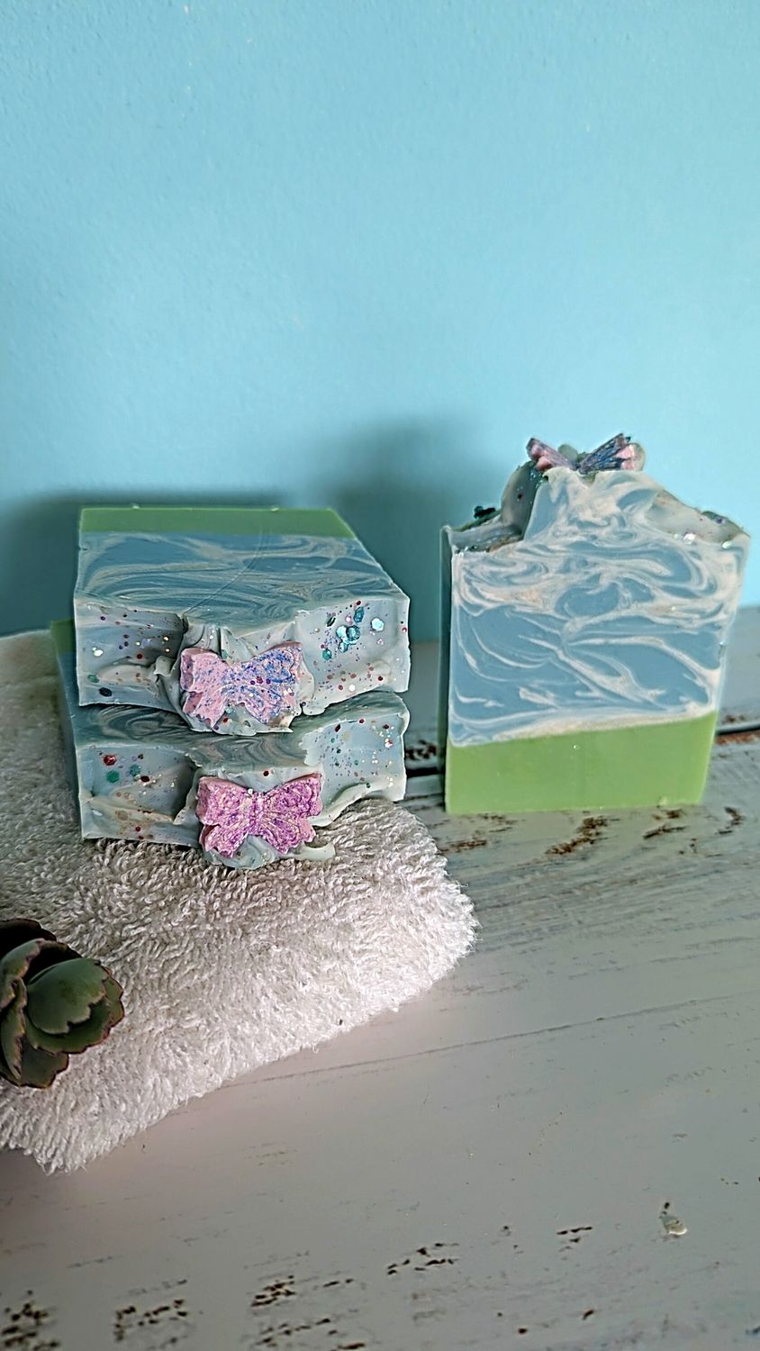 Primavera en Vuelo Soap Decorative boxes with butterfly accents on a textured surface against a blue background.