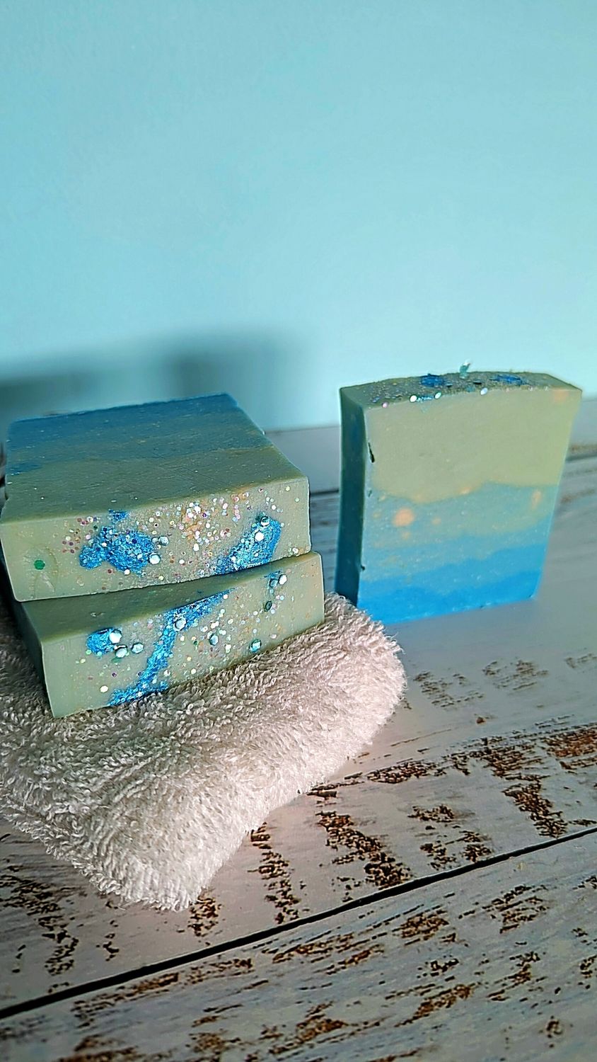 Savia Salpicada Soap Two stacked soap bars with blue and green patterns next to a fluffy white towel.