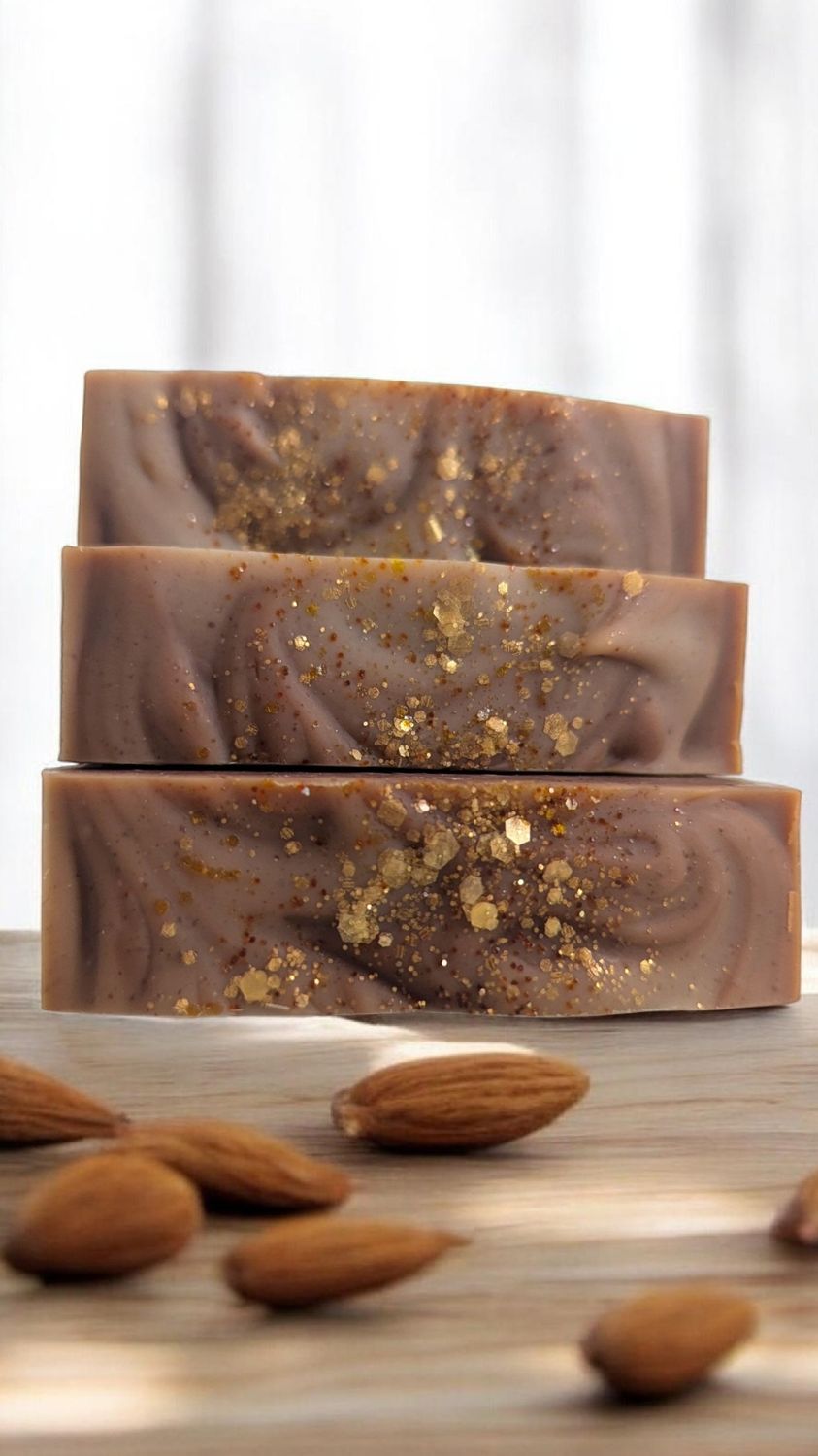 Almond Escape Soap Three stacked bars of brown soap with almond pieces and a textured surface, surrounded by almonds.